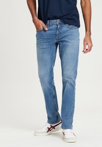 Lichtblauwe denim jeans met een rechte pijpdesign, voorzien van vijf zakken en subtiele whiskering; gedragen met witte sneakers.