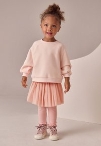 Sweatshirt rose clair à manches larges, assorti à une jupe plissée rose clair. Leggings et baskets complètent la tenue, avec des lacets décoratifs.