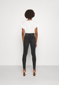 Haut blanc à manches courtes avec détail œillet dans le dos, associé à un jean skinny foncé taille haute et des talons beiges à semelle épaisse en bois.