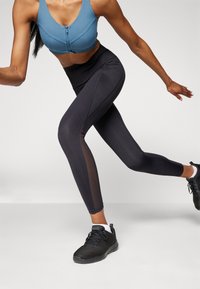 Blue zip-up sports bra paired with high-waisted black leggings featuring mesh panels, complemented by black athletic shoes.