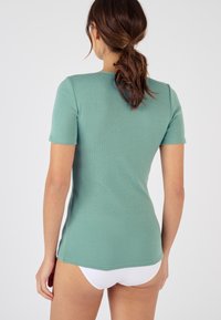 Short-sleeve top in a soft mint green color, featuring a fitted design, ribbed texture, and side slits at the hem.