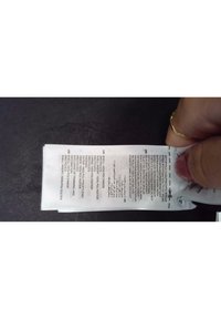 Biała metka z instrukcjami pielęgnacji i informacjami o materiale. Czarne napisy zawierają szczegóły w kilku językach.