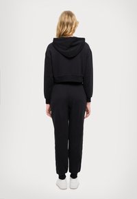 Felpa nera cropped con cappuccio, abbinata a pantaloni jogger neri e sneakers bianche. Tessuto morbido, vestibilità rilassata, polsini a coste alle caviglie.
