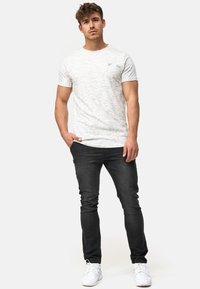 Hellgraues, strukturiertes T-Shirt mit rundem Halsausschnitt und kleinem Logo, kombiniert mit dunklen Slim-Fit-Jeans und weißen Sneakers.