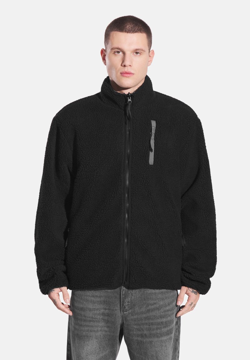 Czarna polarowa kurtka z wysokim kołnierzem, przednim zamkiem błyskawicznym i subtelnym teksturowanym wzorem. Posiada czarny zamek ozdobny na piersi.