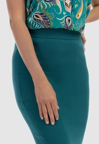 Fustă tricotată teal cu un design ajustat și talie ribrată. Textură netedă, care subliniază forma corpului, asortată cu un top cu model.