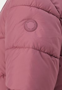 Lyserød pufferjakke med et rundt mærke, quiltet tekstur og blød finish. Designet med en let oversized silhuet.