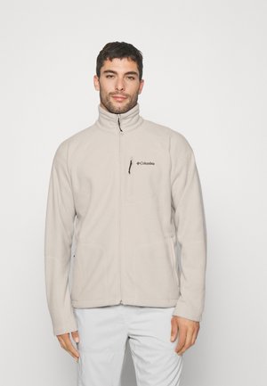 Beige fleece jacket with a high collar, zippered front, and side pockets. Features the Columbia logo on the chest. Soft texture.