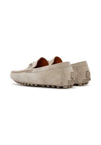 Mocasines de ante beige con un diseño cosido, forma redondeada y suela de goma. Presentan un sutil detalle de logo y bordes texturizados.