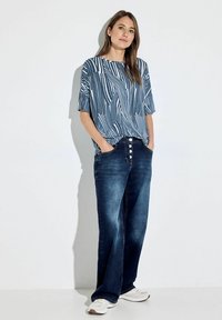 Blauw-witte gestreepte top met korte mouwen gecombineerd met donkerblauwe wijde jeans. Opvallende details zijn de knoopaccenten op de tailleband en witte sneakers.