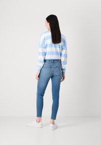 Chemise rayée bleu clair et blanche à manches longues associée à un jean bleu ajusté. Des baskets blanches complètent la tenue.