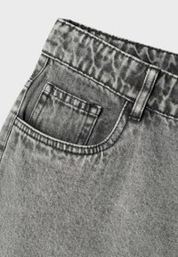 Jean en denim gris avec une texture délavée, comportant une poche arrière et des passants de ceinture. Motif subtil visible dans le tissu pour un détail supplémentaire.