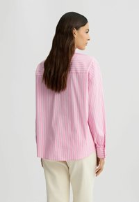 Chemise à manches longues rayée rose et blanche, avec des poignets boutonnés, ourlet légèrement arrondi, en tissu léger, vue de dos.