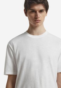 Hvid kortærmet t-shirt lavet af et letvægts, struktureret materiale med rund halsudskæring og en afslappet pasform.