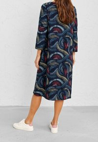 Merimustas mekko, jossa on kolmanneksen pituisten hihnat ja kieppuva monivärinen abstrakti kuvio. Yhdistetty valkoisiin lenkkareihin.