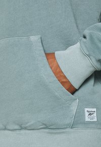 Melerad mintgrön sweatshirt med en känguruficka, ribbade muddar och en liten Reebok-etikett med texten "Natural Dye".