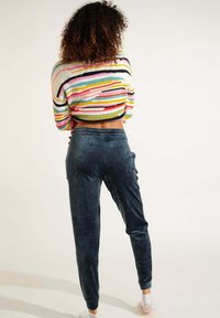 Bunt gestreiftes, gestricktes, kurzes Sweater mit langen Ärmeln, kombiniert mit dunklen Samtjoggern mit glatter Textur und elastischem Taillenbund.