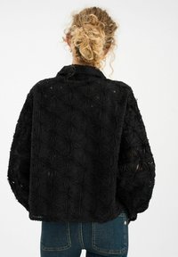 Crna teksturirana jakna s cvjetnim vezom, slobodnog kroja i ovratnikom. Tkanina ima tkan izgled s više slojeva, ističući detalje.