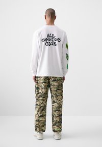White long-sleeve shirt with "ALL CONDITIONS GEAR" printed on the back, paired with camo cargo pants featuring green accents and pockets.