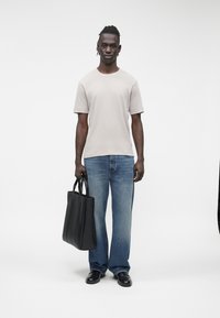 Tricou bej cu mâneci scurte, blugi albaștri largi, pantofi negri din piele, ținând o geantă tote neagră. Design și textură simple, moderne.