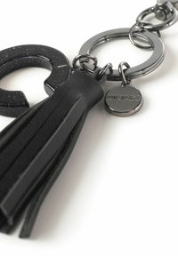 Llavero con un fleco de cuero negro, un acento circular de plata y una forma estrellada negra brillante. Incluye una etiqueta metálica grabada con "MIRIADA."