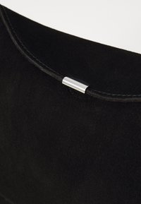 Pochette en daim noir avec une texture lisse et un accent métallique argenté sur la couture supérieure. Design minimaliste sans motifs supplémentaires.