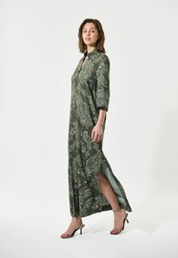 Groene maxi-jurk met een paisleypatroon, kraag en driekwart mouwen. Bevat zijsplitten en een vloeiende stoftextuur.