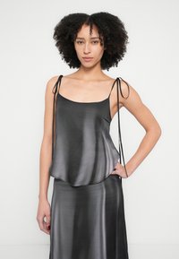 Camisolă neagră din satin cu bretele reglabile, având o formă fluidă și un luciu subtil. Textură netedă, design minimalist.