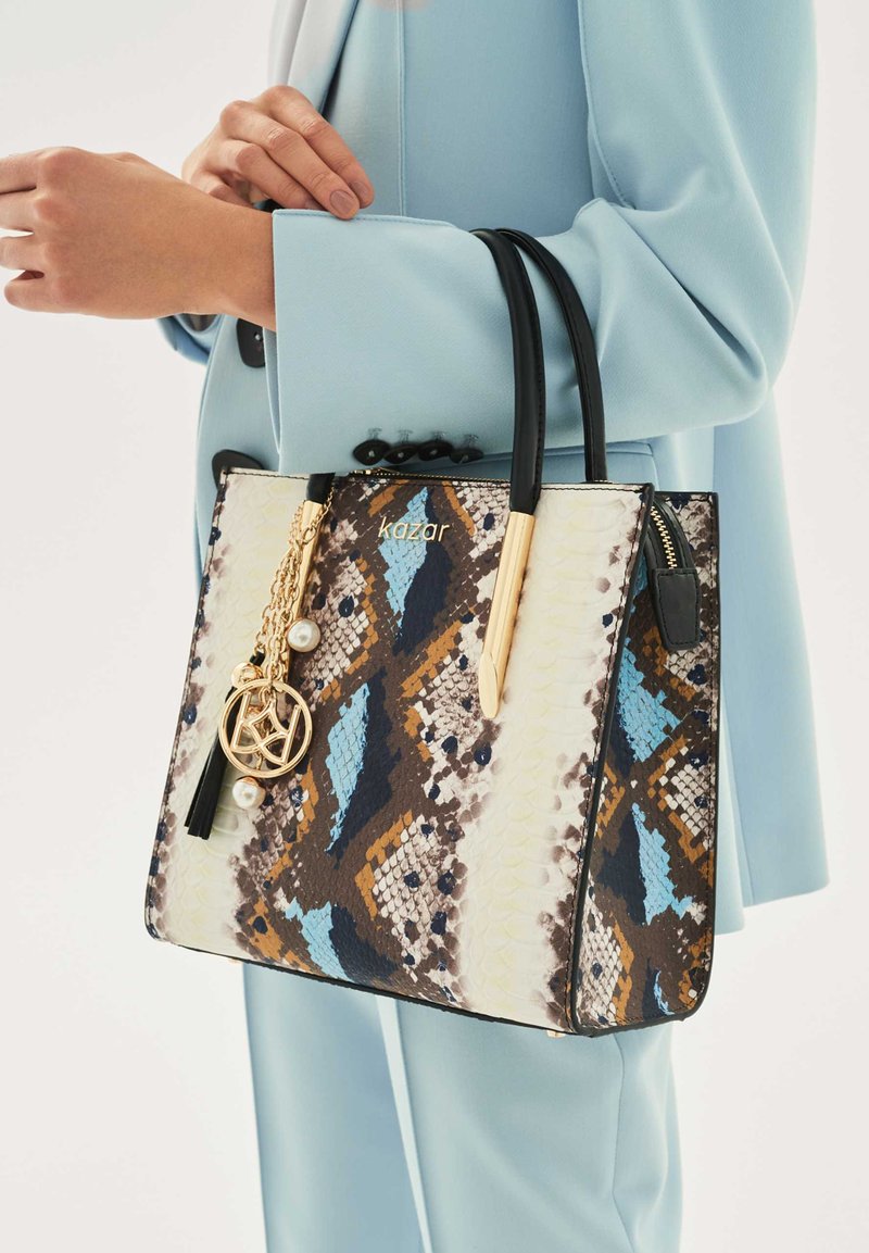 Raštuota nešioklė su mėlynos, rudos ir kreminės spalvų gyvatės odos raštu, su juodais odiniais rankenomis ir aukso spalvos metalo detalėmis.