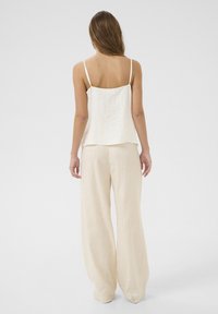 Cream-colored, flowing camisole with thin straps, paired with beige, wide-leg linen trousers, showcasing a relaxed silhouette.