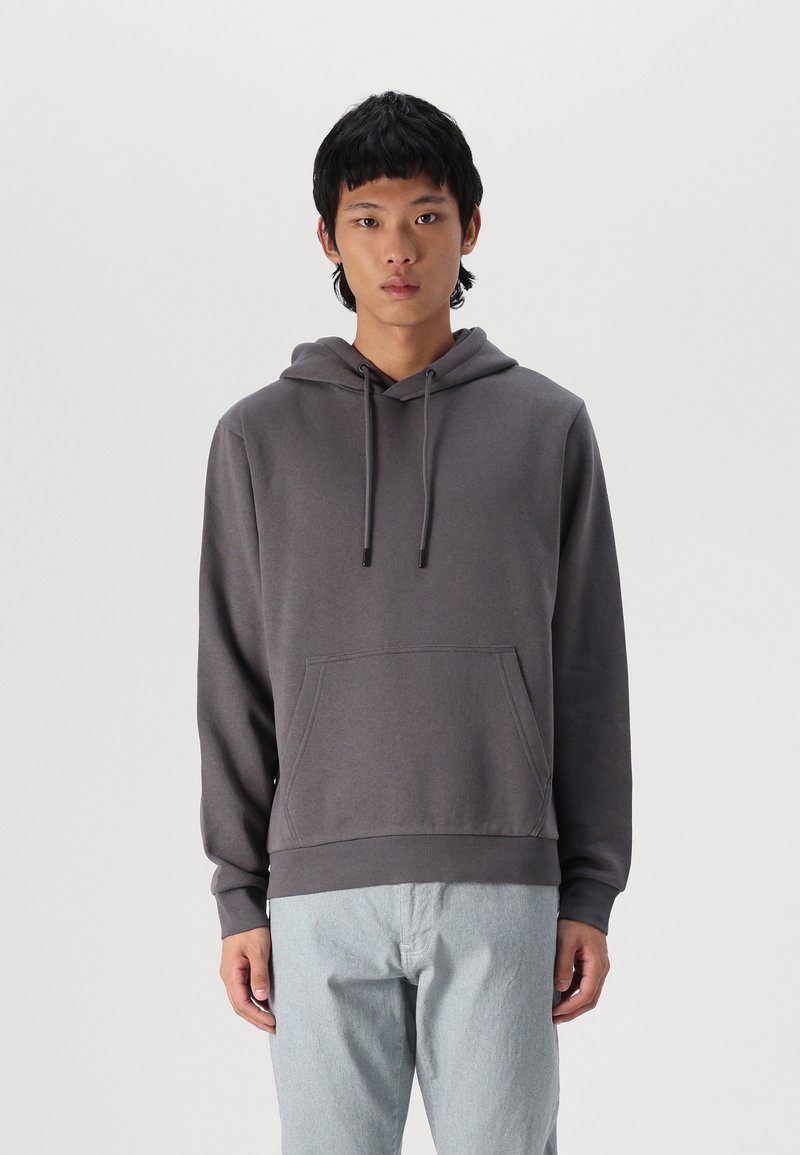 Grijze sweatshirt met een capuchon, verstelbare koordjes en een voorzak; de stof lijkt zacht met een gladde textuur; gedragen met lichtblauwe broek.