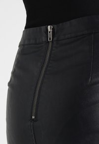 Jupe en cuir noir avec une fermeture éclair en argent visible sur le côté gauche, au toucher lisse et au design ajusté.