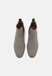 Un par de botas Chelsea de ante gris con paneles laterales elásticos negros y lengüetas, vistas desde arriba sobre un fondo blanco.