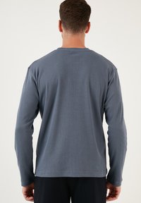 Camisa de manga larga en un tono azul apagado, con textura acanalada y un cuello redondo clásico. Diseño simple, sin logotipos o acentos visibles.