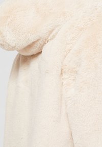 Primer plano de una suave tela de pelo sintético de color crema, con una textura y pliegues visibles, que sugieren calidez y una suavidad lujosa.