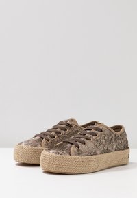 Baskets beiges avec des dessus ornés de sequins, lacets plats marron et semelles en jute, offrant une surface texturée et un design décontracté.