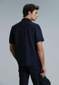 Korte mouwen marineblauwe shirt van linnen, met een ontspannen pasvorm, kraag en subtiele textuur. De achterkant toont stiksels en geen zichtbare knopen.
