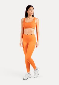Ensemble de vêtements de sport orange composé d'un crop top ajusté et d'un legging taille haute, tous deux en matière lisse et extensible. Baskets blanches.