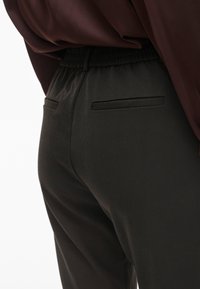 Črne hlače iz elastičnega materiala z elastičnim pasom, ki imata dve zadnji žepu z elegantnim obrobo. Gladka tekstura, prilegajoč kroj.