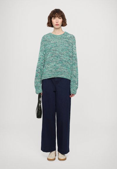 Textured green knit sweater with long sleeves, paired with wide-leg navy pants and beige shoes. A small black handbag complements the outfit.