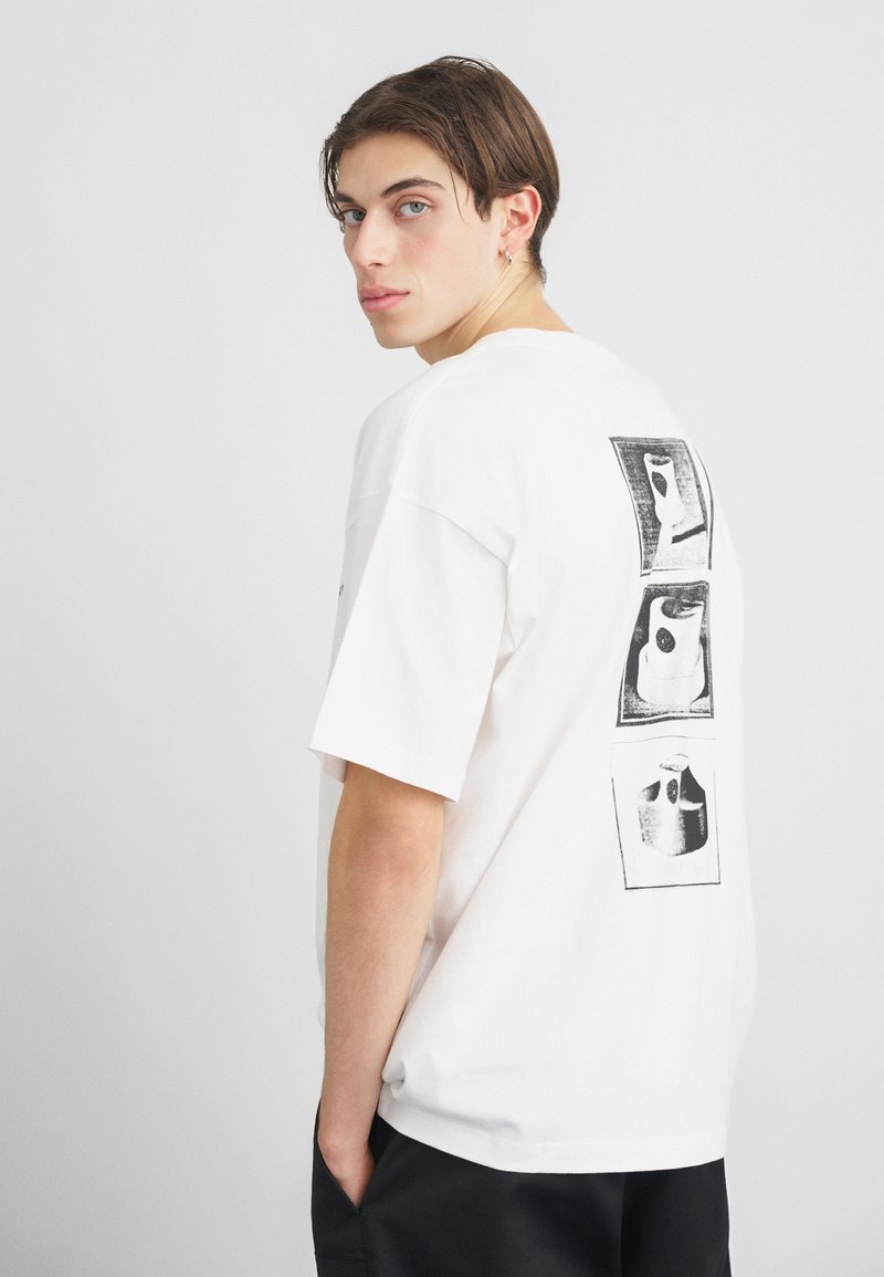 Camiseta blanca de algodón con tres estampados gráficos en la parte posterior. Corte holgado con mangas cortas y un escote redondeado.