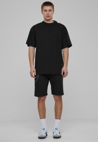 Crna oversized majica kratkih rukava s okruglim izrezom u paru s crnim kratkim hlačama koje imaju srebrni lanac i bijelim sportskim čarapama.