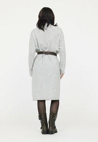 Graues gestricktes Kleid mit tailliertem Gürtel, langen Ärmeln und knielanger Silhouette, kombiniert mit schwarzen Lederstiefeletten.