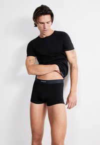 Černé boxerky SLOGGI s tmavým elastickým pasem a ladícím černým priléhavým tričkem, obojí vyrobené z hladkého, elastického materiálu.