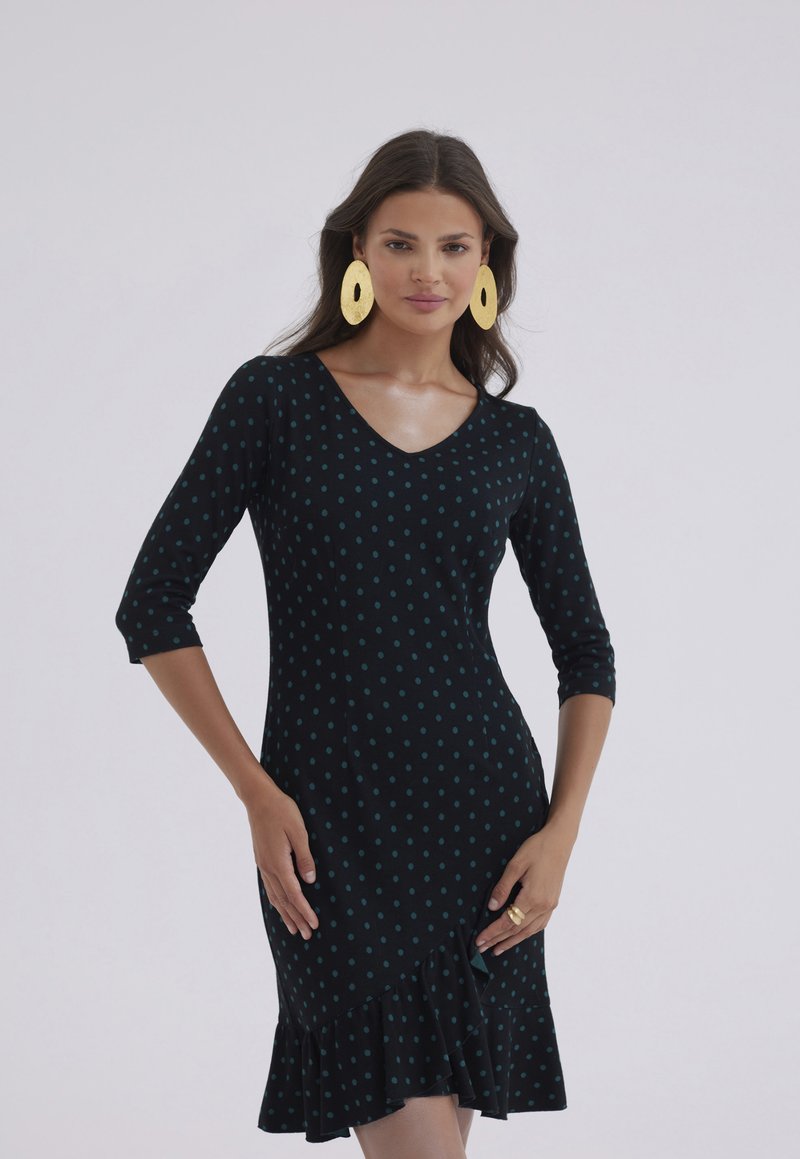 Czarna sukienka w turkusowe kropki, dekolt w serek, rękawy trzyczwarte i falbaniasty dół. W zestawie duże, złote owalne kolczyki. Gładka tekstura.