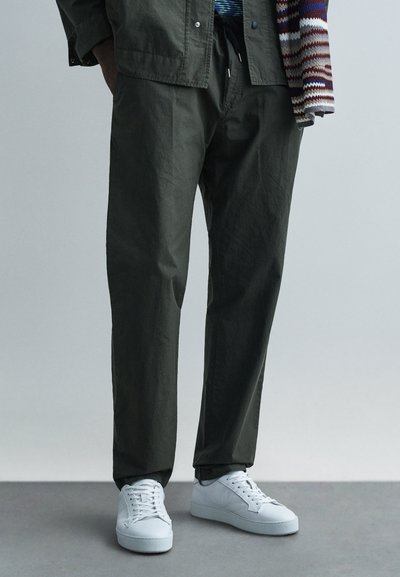 Pantalon en coton vert olive à coupe décontractée, associé à des baskets blanches avec une tige texturée et des semelles plates.