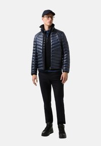 Námorní pufovací bunda s horizontálním prošíváním, vysokým límcem a zipem. Kombinována s černým svetrem, námořnickými kalhotami a černými vysokými teniskami.