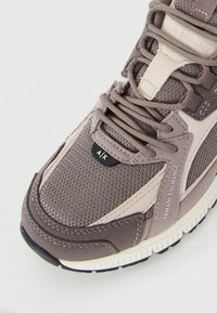 Sneaker-uri gri și bej Armani Exchange cu partea superioară din plasă, suprapuneri din piele întoarsă, etichete branduite și sireturi, pe un fundal alb.