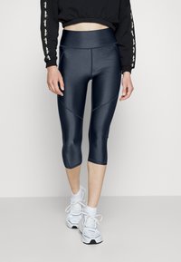 Laivastonsiniset, korkeavyötäröiset capri-leggingsit, joissa on sileä, kiiltävä pinta ja sauma-yksityiskohtia. Yhdistetty valkoisiin urheilutennareihin.