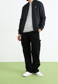 Black bomber jacket with a subtle pattern, gray ribbed sweater, black trousers, and white sneakers. Smooth fabric and relaxed fit.